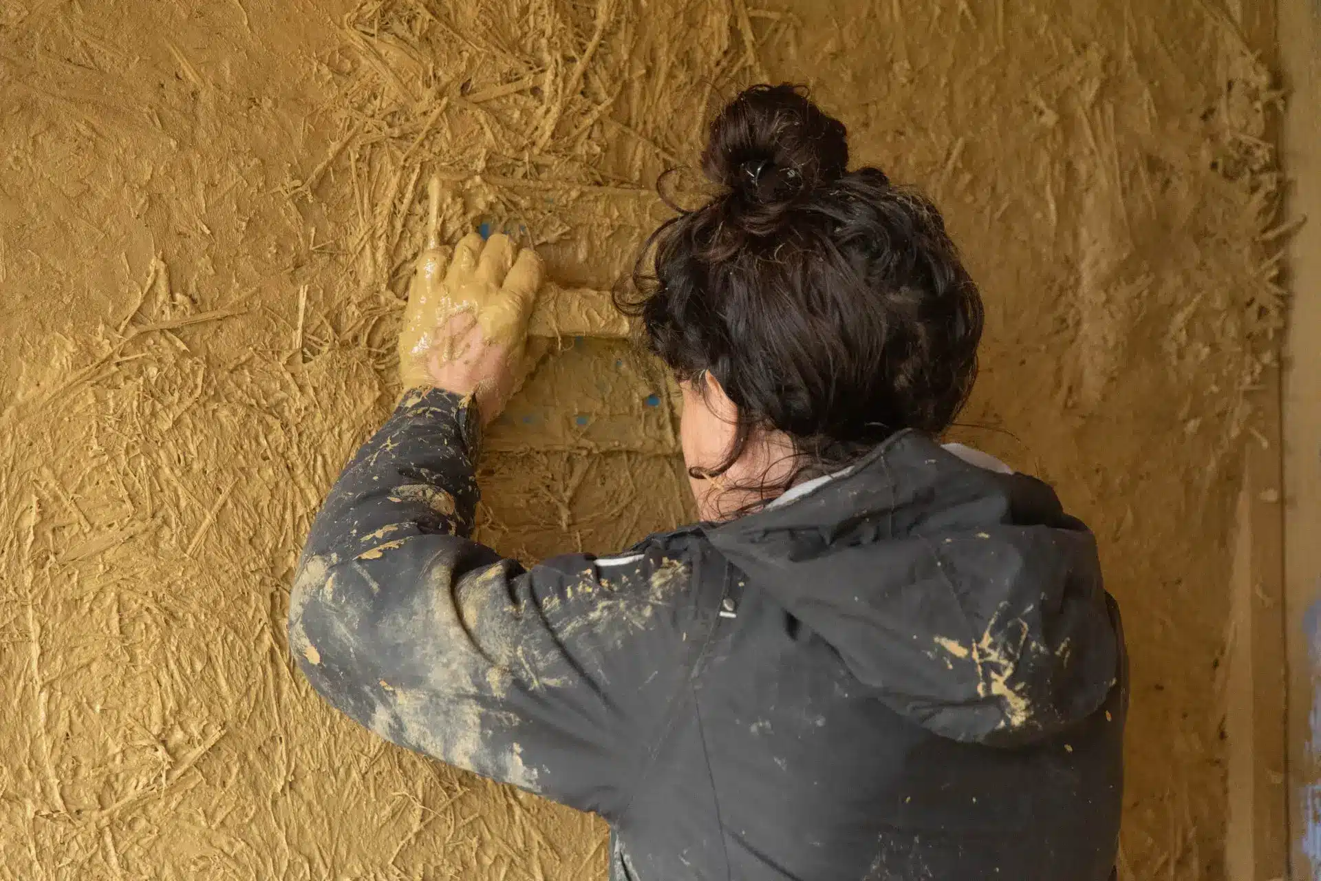 une personne étale un enduit en paille chanvre sur un mur Al'Terre Égaux pendant une formation transition écologique jeune formations longues Al’Terre Égaux